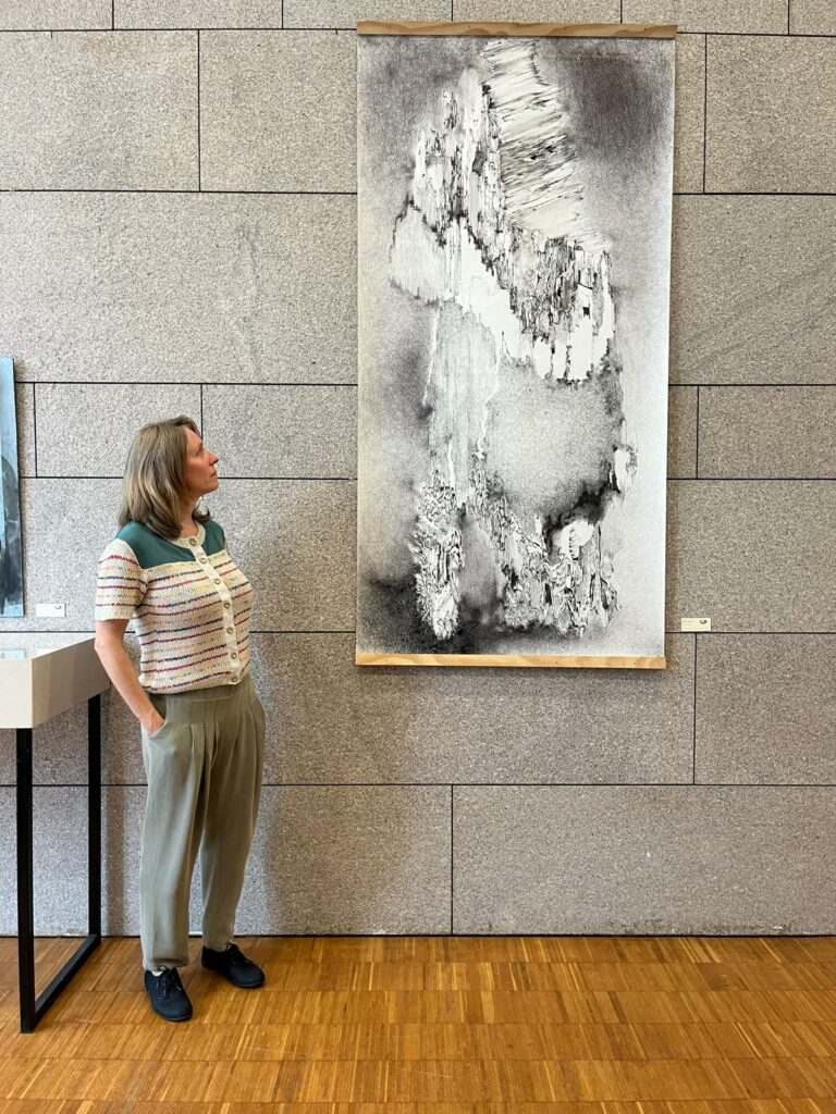Portrait de l'artiste Natacha Baluteau debout à côté d'un grand dessin contemporain abstrait lors de son exposition vases communicants.