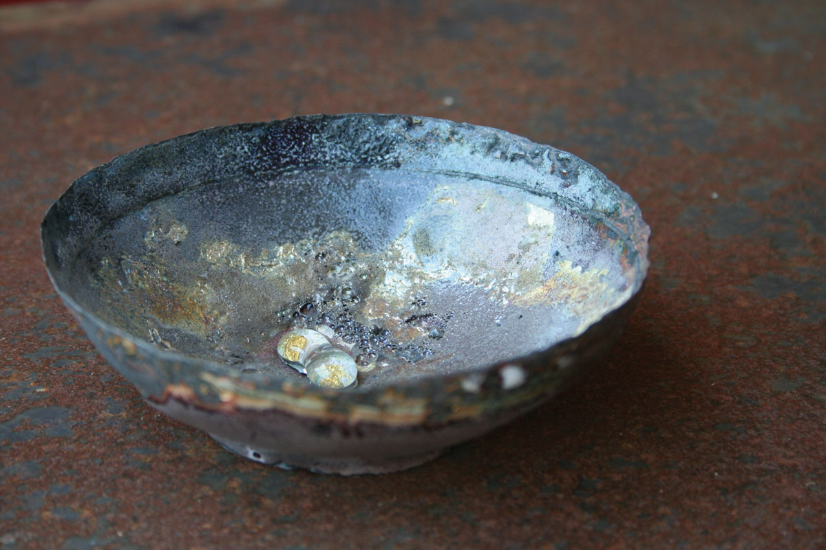 Sculpture en forme de bol de la série Archéo par Natacha Baluteau. Œuvre en émail contemporain sur cuivre de 12x5 cm aux reflets métalliques, irrisés. Au centre on devine des éclats de cristal enfermant en leur centre des éclats d'or. L'objet évoque un vestige précieux découvert lors de fouilles archéologiques.
