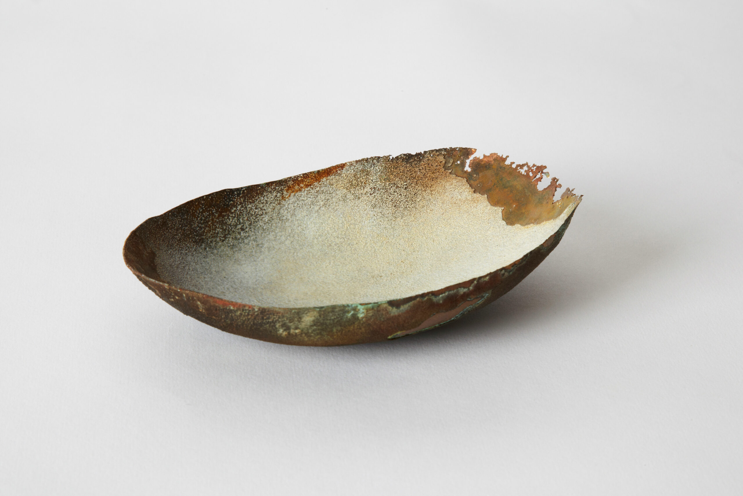 Œuvre d'art contemporain en émail sur cuivre de la série Archéo par Natacha Baluteau. Sculpture en forme de coupe ou de coque oblongue, révélant un intérieur émaillé blanc lumineux et des bordures en metal oxydé, brut et dentelé.
