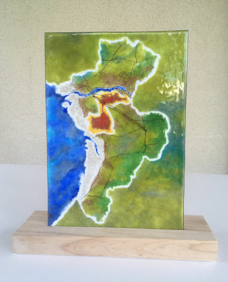Plaque émaillée artisanale réalisée par l'artiste Natacha Baluteau. En cuivre émaillé, elle représente l'imbrication de deux cartes, l'ensemble se compose de dominantes vertes et bleus. On aperçoit vers le centre des couleurs orangés et rouge. La surface et brillante.