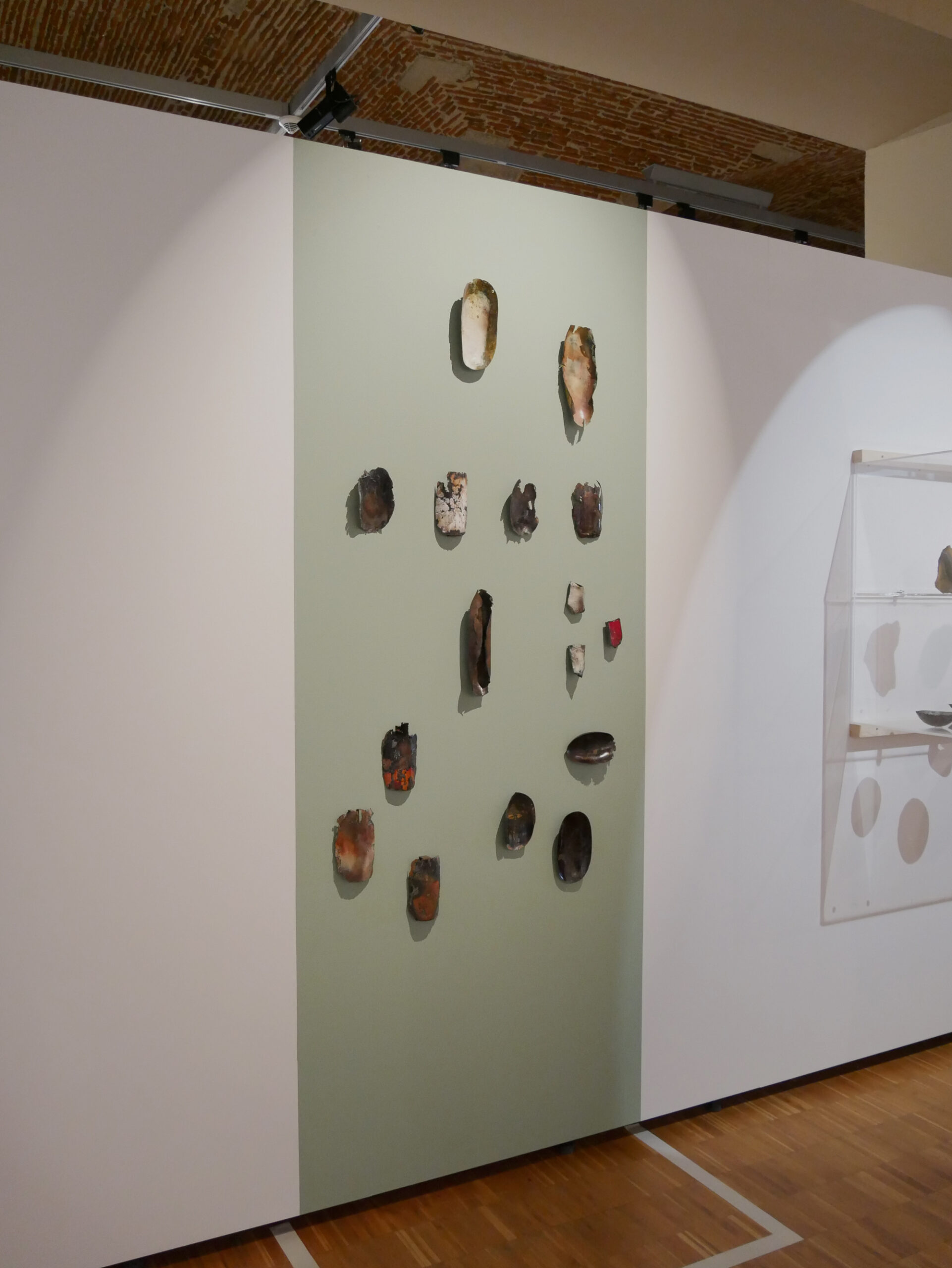 Installation murale de la série Archéo par Natacha Baluteau, présentée lors de l'exposition Dixsemblables à la Galerie des Hospices de Limoges. Sculptures en émail contemporain évoquant des fragments issus de fouilles archéologiques.