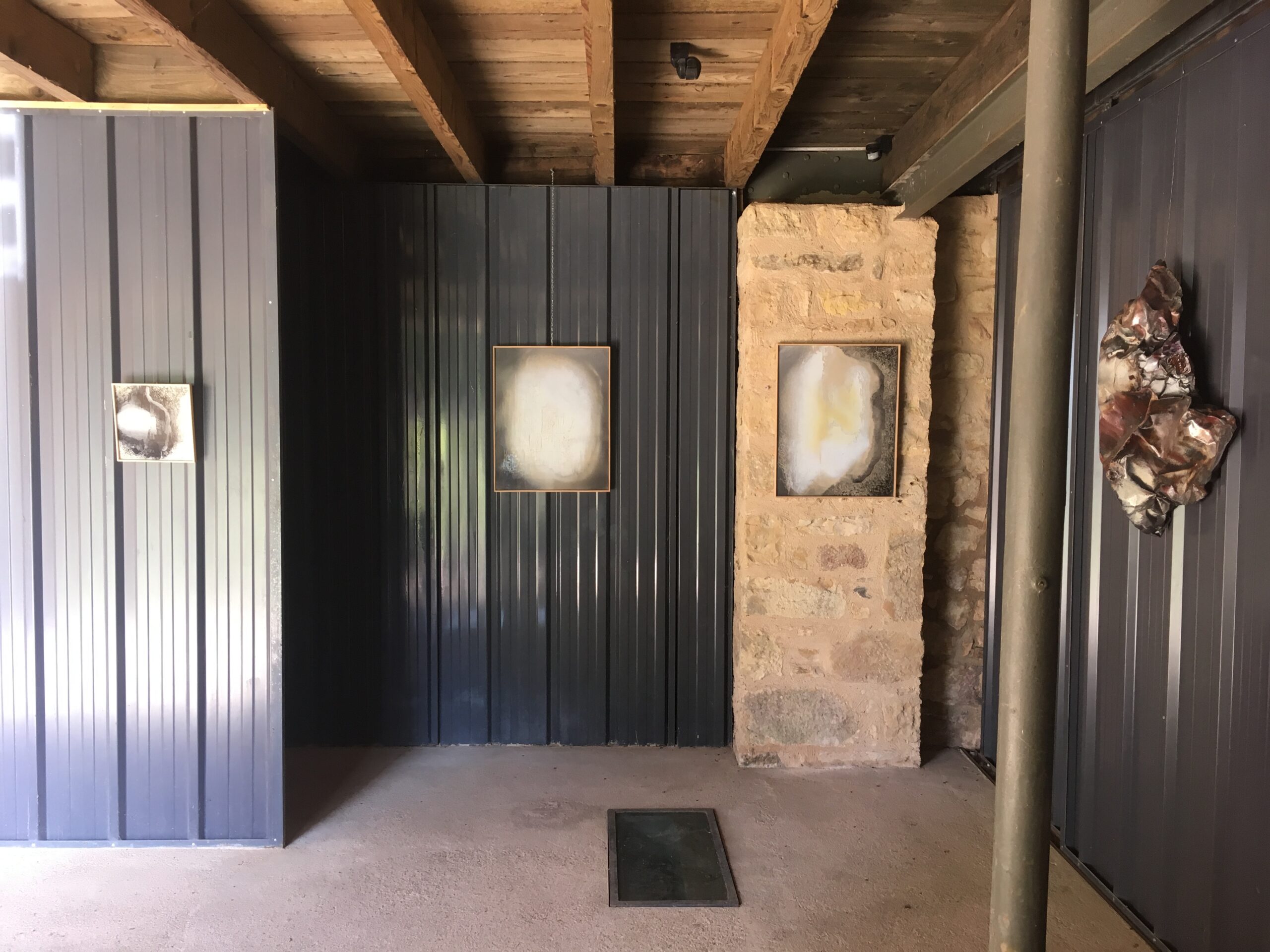 Vue de plaques murales en émaux contemporains de l'artiste Natacha Baluteau, les couleurs sont gris, clairs, sable, ivoire. Sur la droite de l'image une sculpture en métal martelé aux couleurs, ocre, terre sombre.