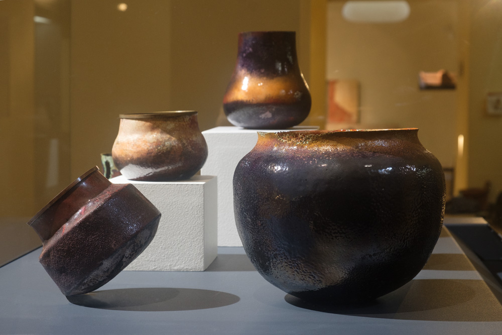 Vue de plusieurs vases réalisés en émail de Limoges par l'artiste plasticienne Natacha Baluteau. De couleurs violet, mordorés, jaunes cerclés de laiton et aux bordures dentelées. Présentation lors de l'exposition Vases communicants au Musée des Beaux-Arts de Limoges.
